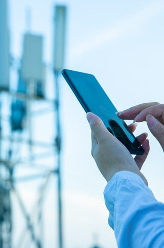 Hands holding phone, in background is a telephone mast